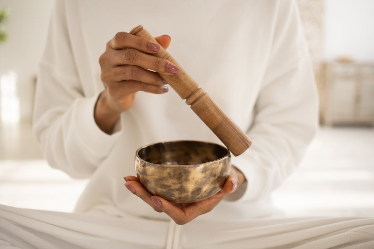 A woman uses a Tibetan singing bowl for meditation and relaxation indoors.